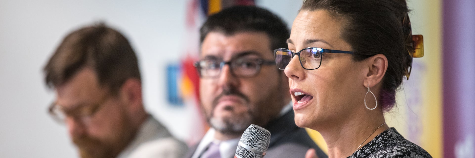 woman speaking into a microphone next to two men