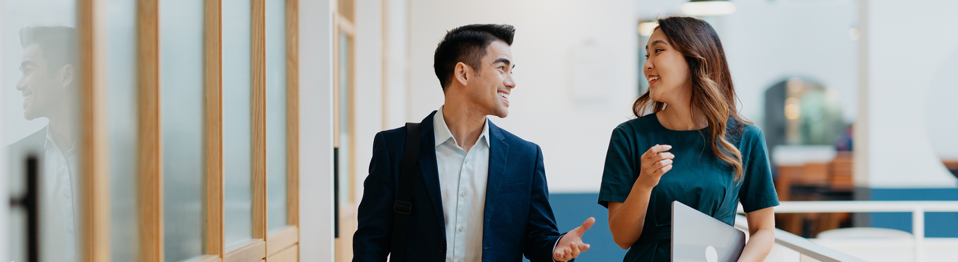 two businesspeople walking and talking in a hallway while holding computers