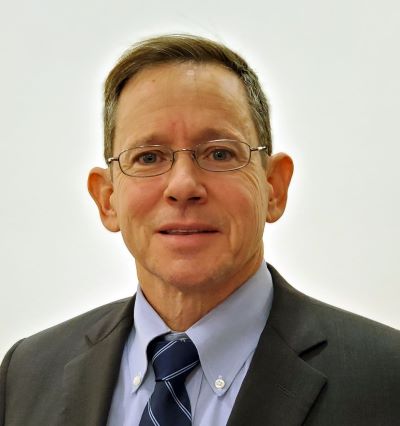 Craig Sullivan headshot - fair-skinned man, brown hair, glasses, blue collared shirt, gray suit, navy and white striped tie