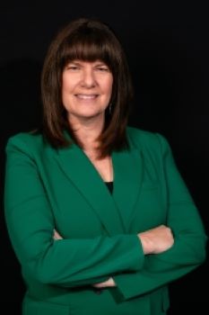 Kari Kent headshot - fair-skinned woman, smiling, brown hair, green blazer, black shirt