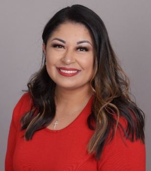 Brandi Flores headshot - medium-skinned woman, smiling, brown hair, red sweater, necklace