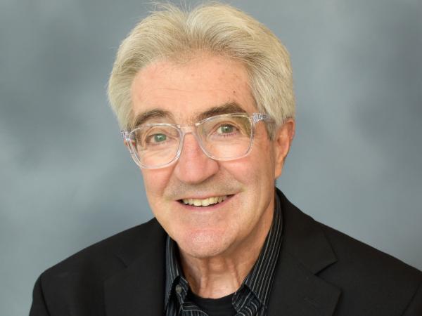 Morris Fiorina headshot. White man. Early 70s. Black jacket and purple button down. Clear framed glasses.