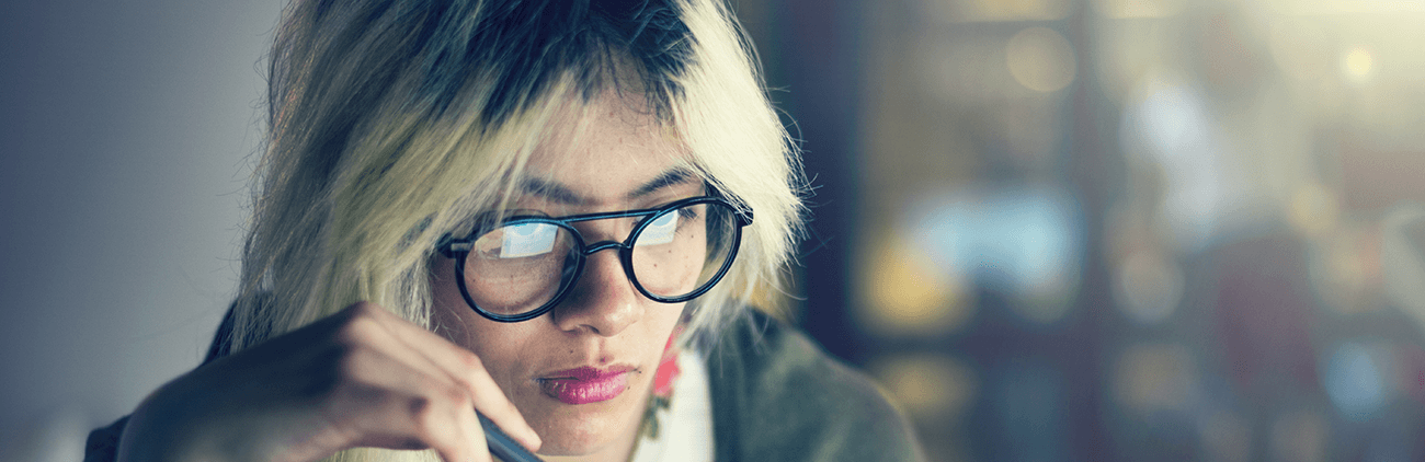 student with glasses and blond hair holding a pen and looking at a computer