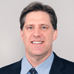 Brian Gerber headshot - fair-skinned man, smiling, black hair, blue collared shirt, navy blazer, navy tie