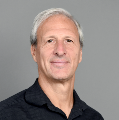 Daniel Schugurensky headshot - fair-skinned man, smiling, gray hair, black collared shirt