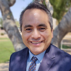 Hector Zelaya headshot - fair-skinned man, smiling, gray hair, blue collared shirt, navy blazer, blue and orange tie