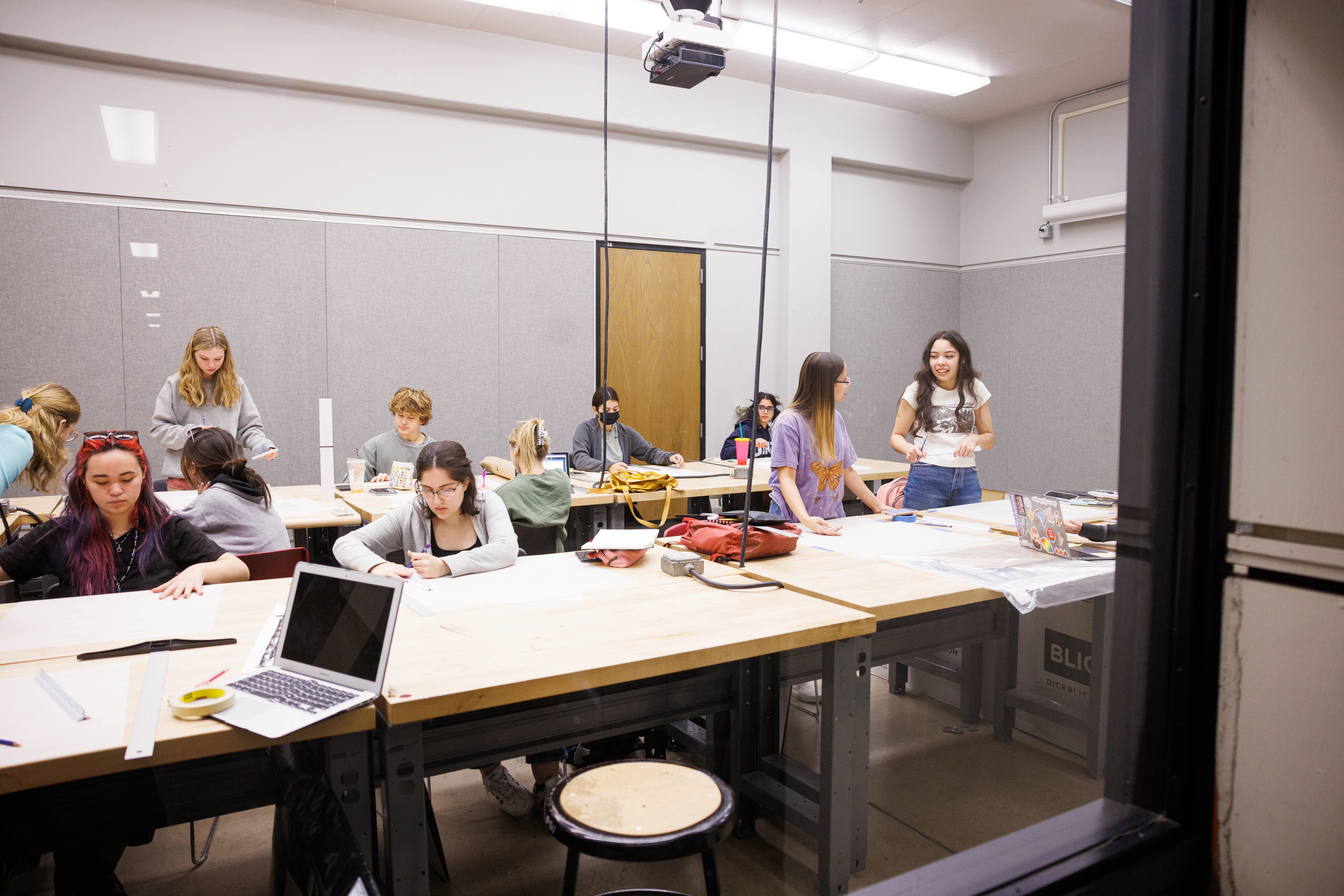 college students sitting and standing around tables covered in backpacks, laptops, and writing utensils