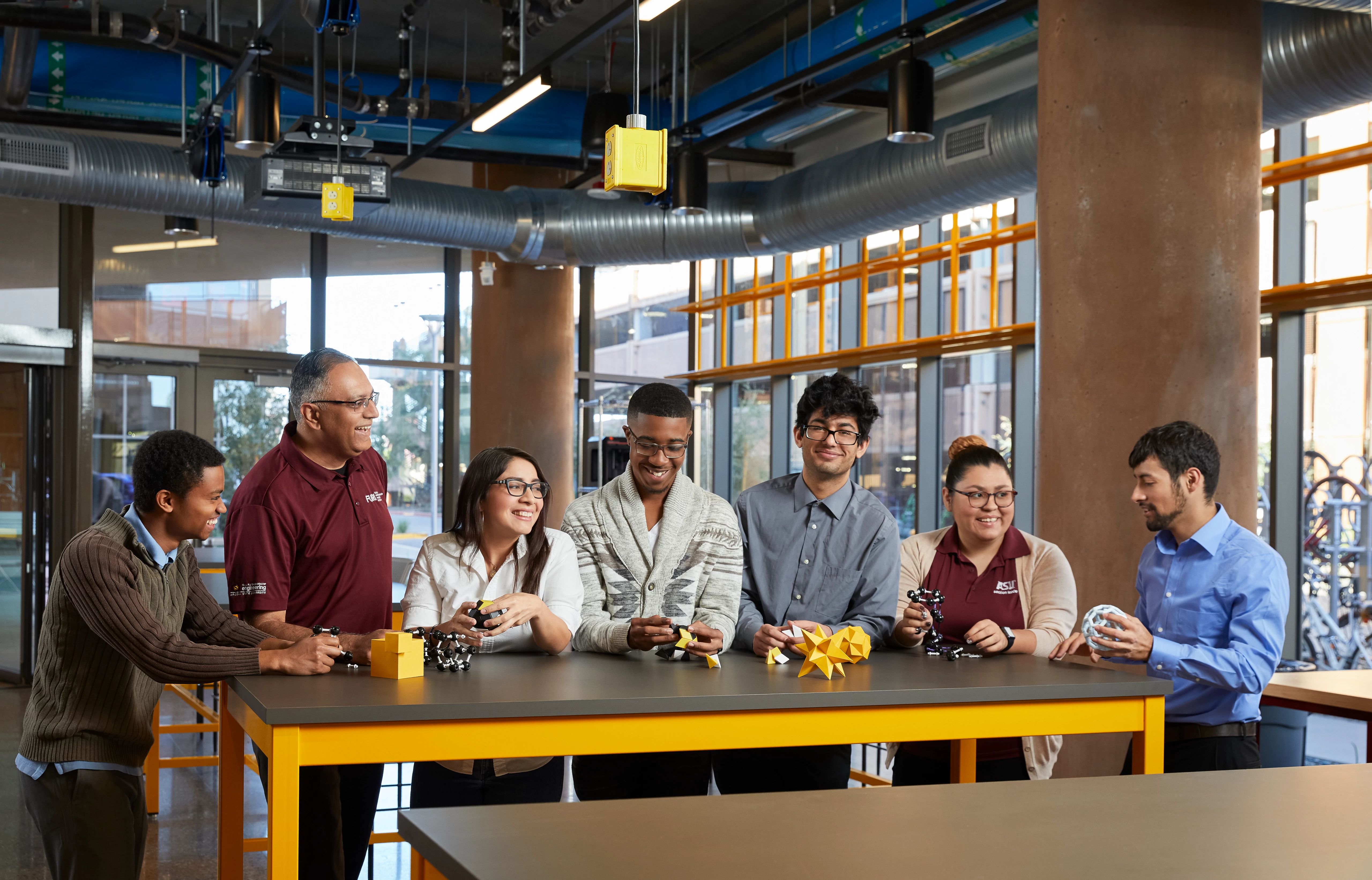 seven SPA alumni standing around a table holding geometric shapes