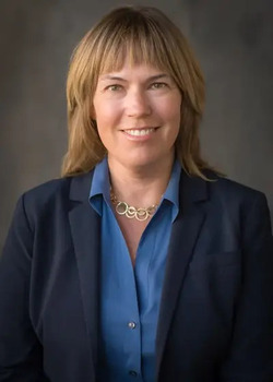 Jen Pokorski headshot - fair-skinned woman, smiling, brown hair, blue collared shirt, navy blazer, necklace