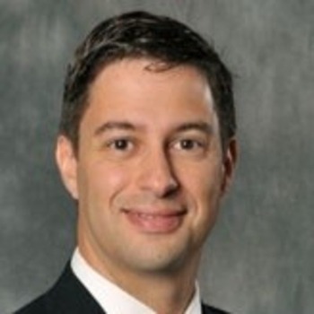 Spiro Maroulis headshot - fair-skinned man, smiling, brown hair, white collared shirt, black blazer