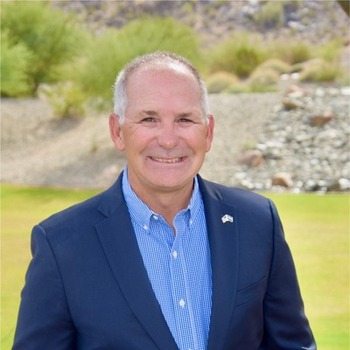 Kelly R. Leid headshot - fair-skinned man, smiling, white hair, blue collared shirt, navy blazer