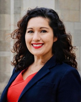 Shannon Portillo headshot - fair-skinned woman, smiling, brown hair, orange shirt, navy blazer, necklace
