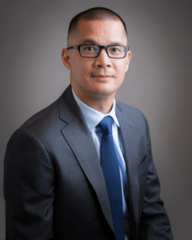 Leo Lew headshot - medium-skinned man, black hair, glasses, light blue collared shirt, gray blazer, blue tie