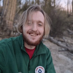 Ethan Clay headshot - fair-skinned man, smiling, blond hair, brown beard, green jacket, red shirt