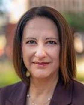 Gina Montes headshot - fair-skinned woman, brown hair, purple blazer, necklace