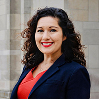 Shannon Portillo headshot - fair-skinned woman, smiling, brown hair, orange shirt, navy blazer, necklace