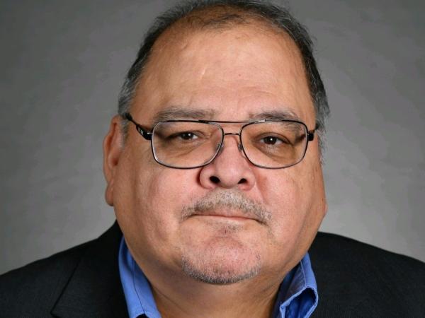 Joseph Garcia headshot. Hispanic male. Late 50s. Wearing a black jacket and blue button up.